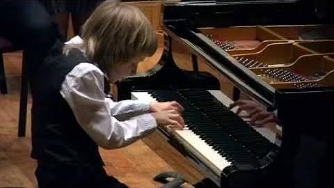 Young Alexander Denisov performing on stage at a grand piano